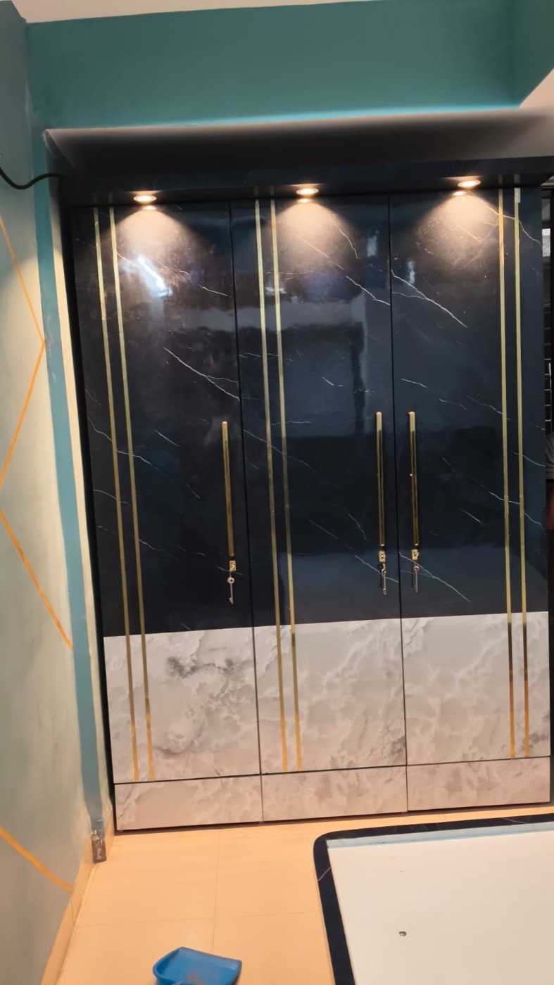 Three-door wardrobe in dark marble-finish laminate with gold profile lines and spotlights.